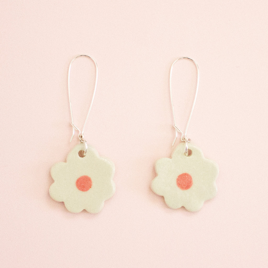 Flower-shaped earrings with a pink center on a light pink background
