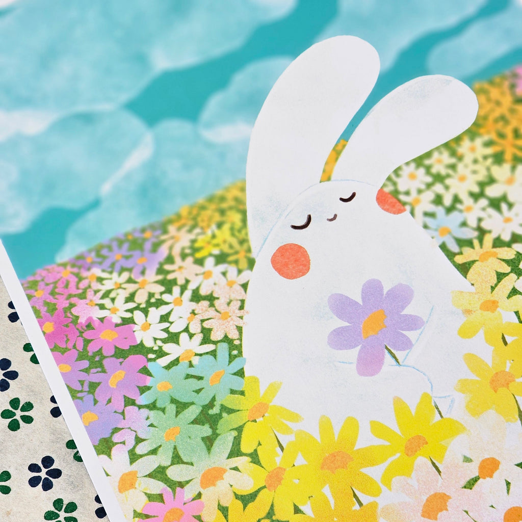 A close-up of a colourful illustrated print featuring a white bunny surrounded by yellow, pink, purple, and green flowers, with a turquoise sky-like background.