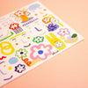 A close-up of a rectangular postcard featuring colourful illustrations with a white background photographed on a peach backdrop. 