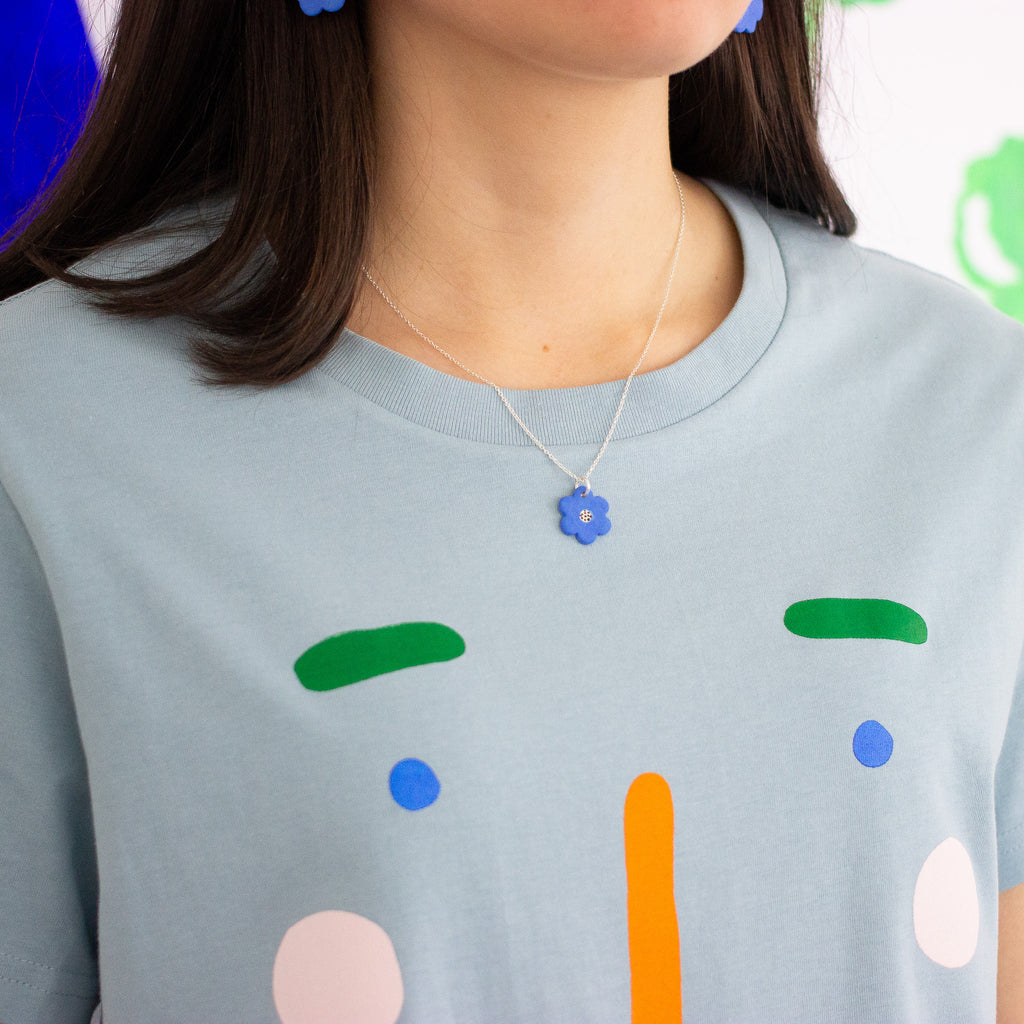 Closeup photo of a person wearing the bright blue flower necklace. Necklace is on a sterling silver chain with a bright blue ceramic bead in a flower shape, with a white and black dotted centre. 