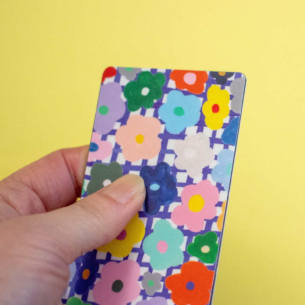 A hand holding a rectangular sticker with a colourful floral pattern against a solid yellow background.
