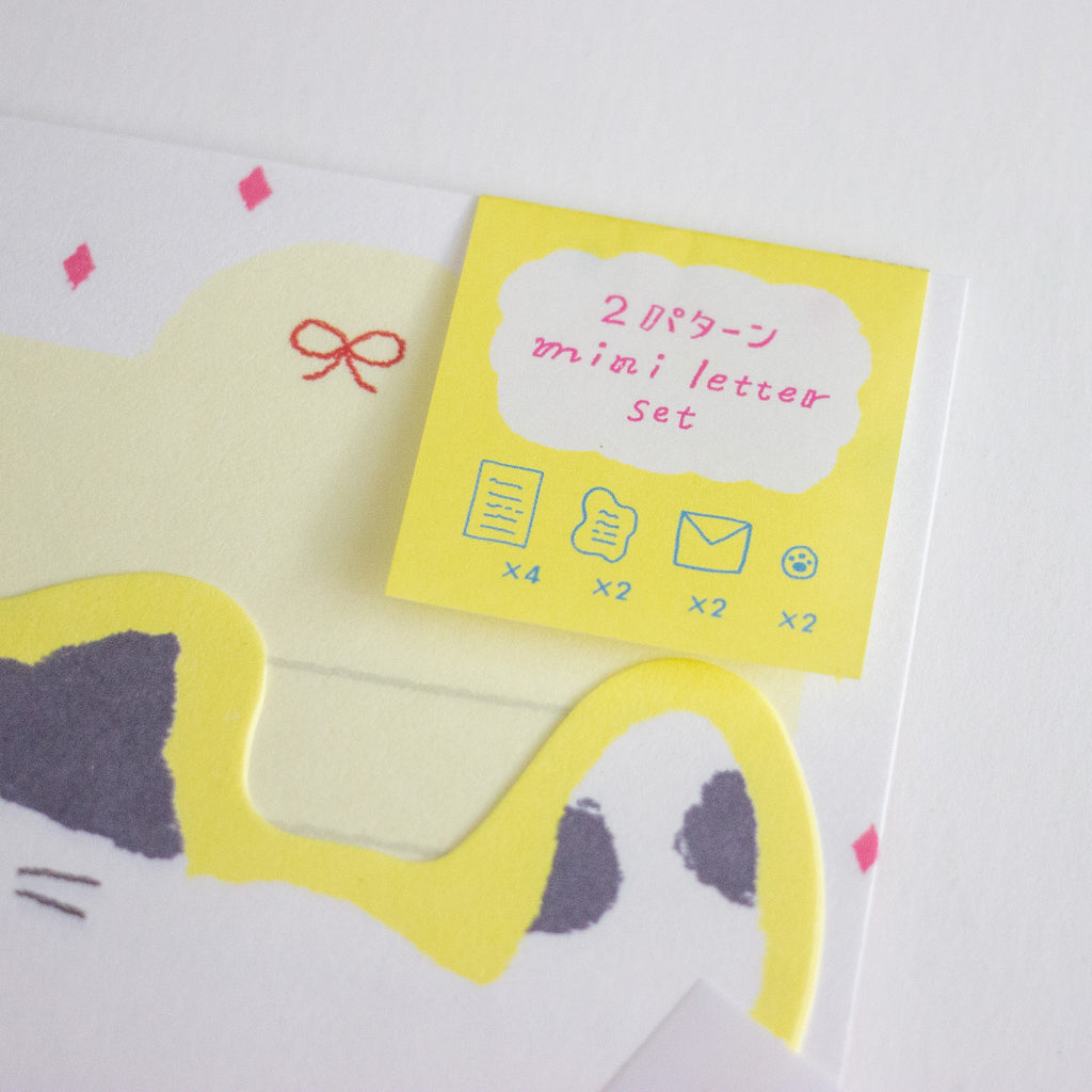 A close-up of a stationery set featuring a bright yellow label labeled '2 mini letter set' on a white card with a yellow cat-shaped border and small pink bow details.