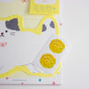 A close-up of a stationery set featuring a white card with a yellow cat outline and a small white sticker sheet with two yellow paw-print designs, set against a white background.