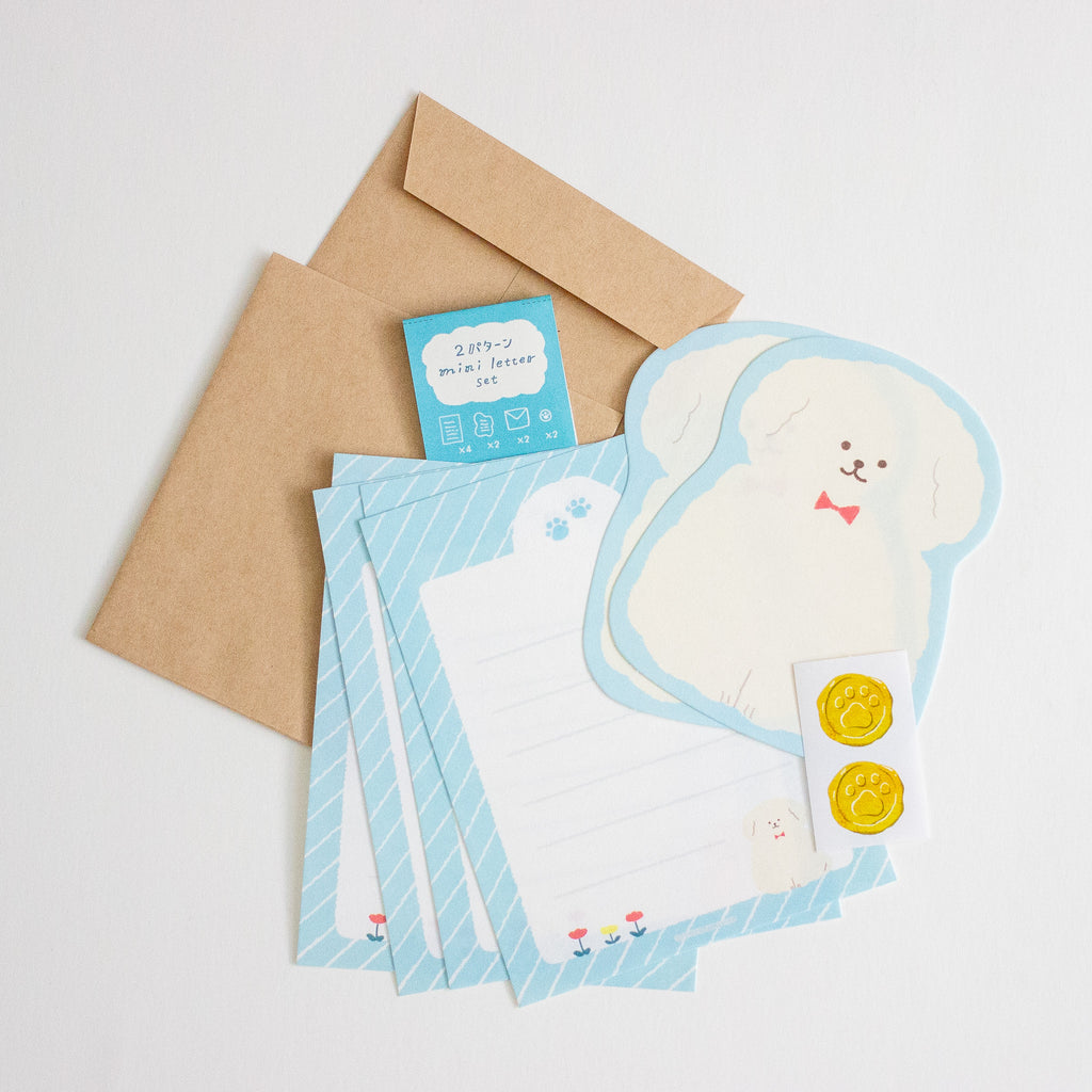 A stationery set laid out on a light grey background, including kraft paper envelopes, light blue striped letterheads, a white die-cut letterhead with a cartoon dog outline, a small blue card, and two round paw gold stickers.