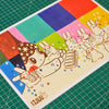 A square art print featuring a whimsical cartoon character with a star-patterned hat and colourful rainbow blocks in the background, placed on a green cutting mat.