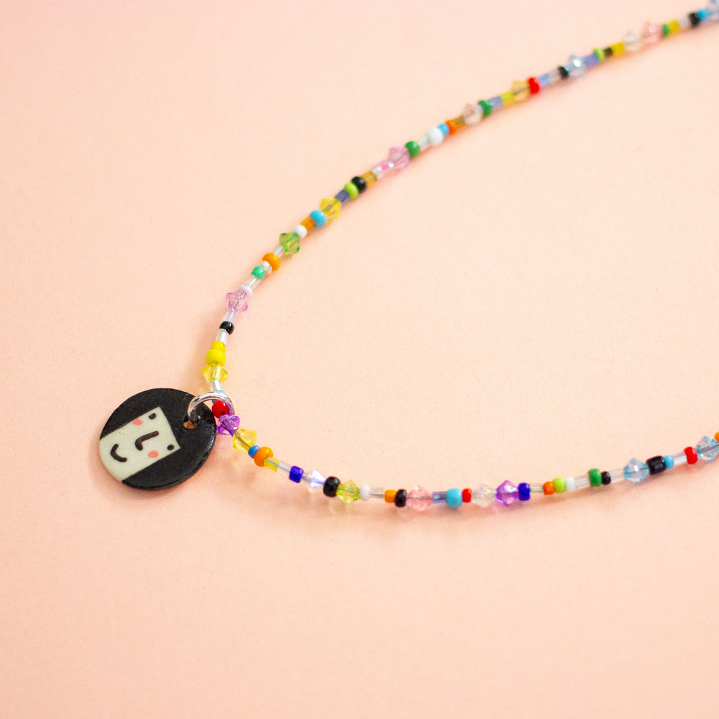 Colourful beaded necklace with a round pendant on a peach background