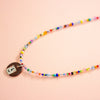 Colourful beaded necklace with a round charm on a pink background