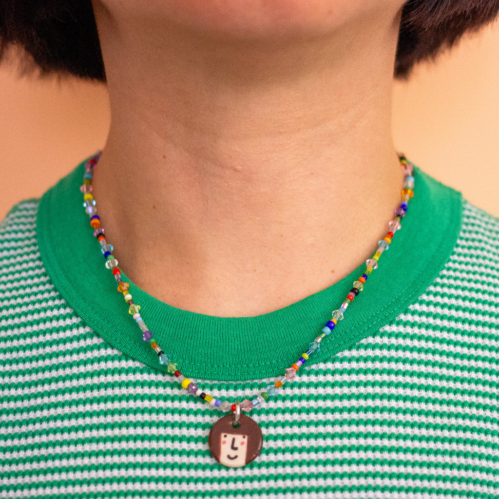 Person wearing a colourful beaded necklace with a pendant on a green and white striped shirt.