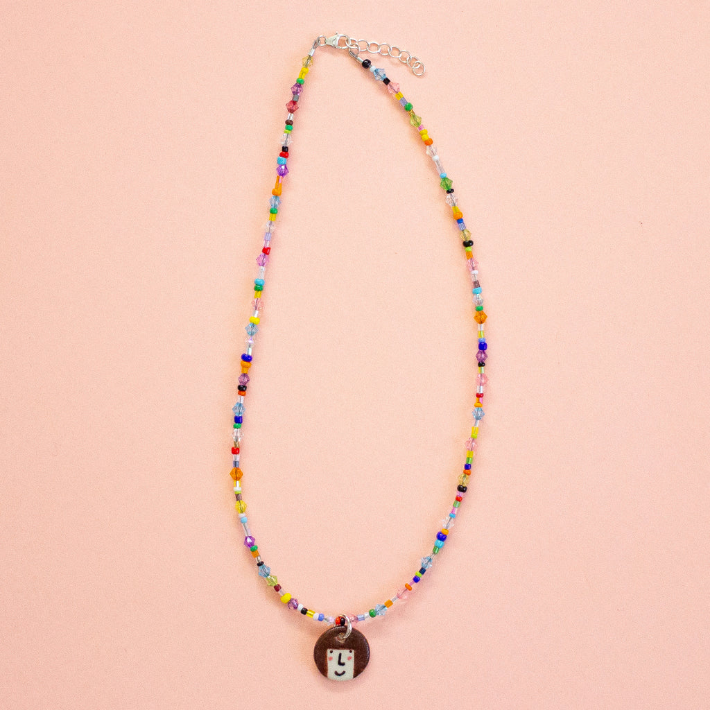Colourful beaded necklace with a round pendant on a peach background