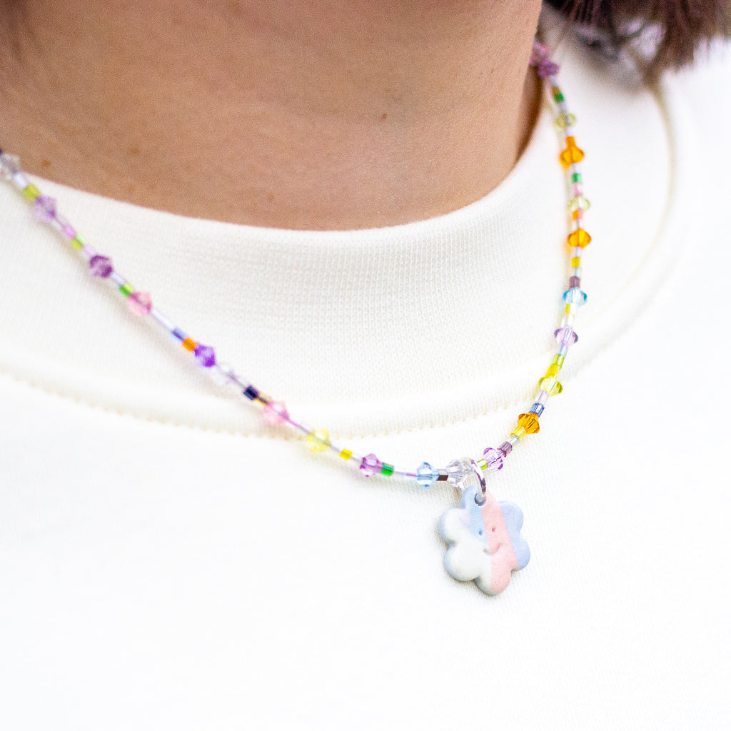 Colourful beaded necklace with a flower charm worn by a person.