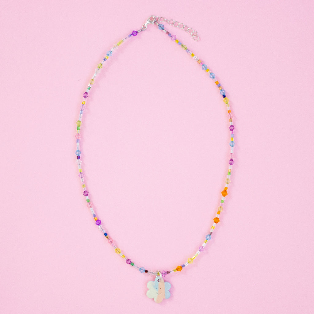 Colourful beaded necklace with a floral charm on a pink background