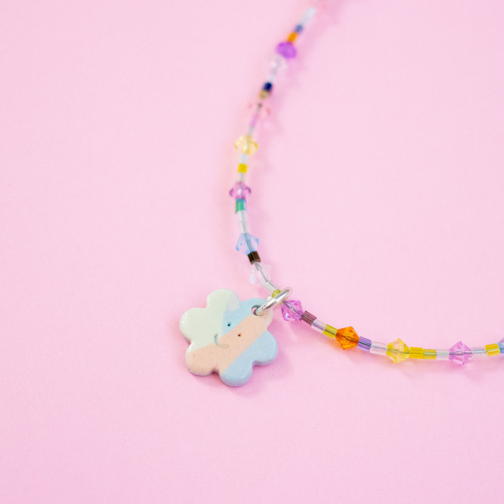 Colourful beaded necklace with a flower-shaped pendant on a pink background