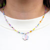 Colourful beaded necklace with a flower charm worn by a person on a white background