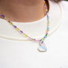 Colourful beaded necklace with a heart-shaped pendant on a cream background