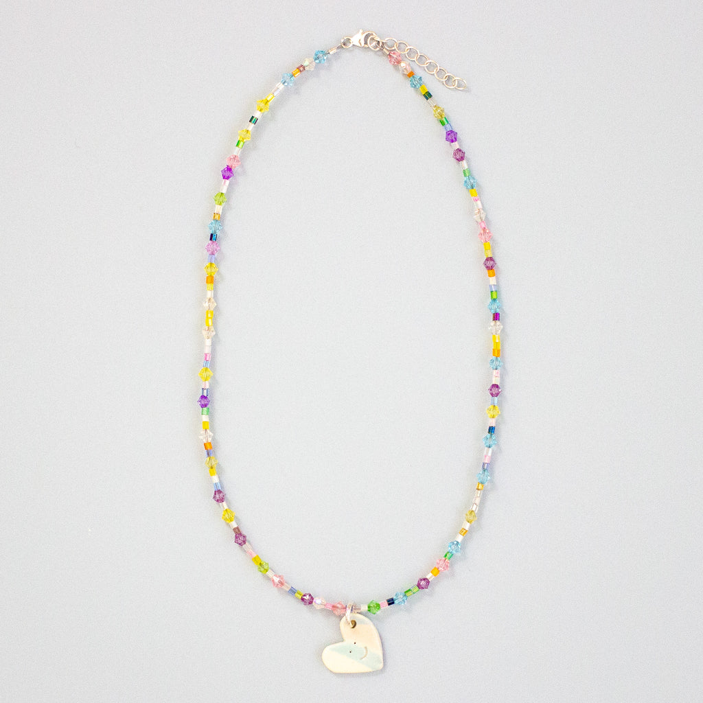 Colourful beaded necklace with a heart-shaped pendant on a light grey background