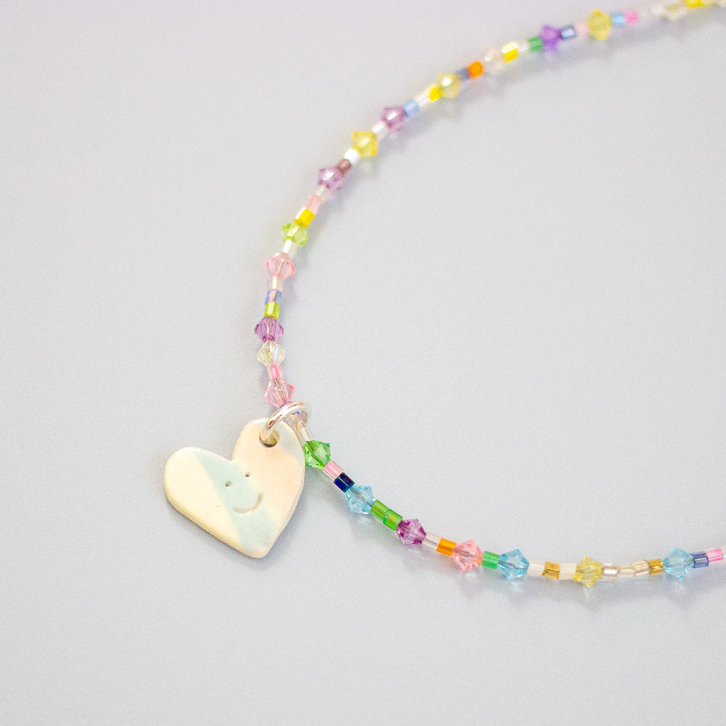 Colourful beaded necklace with a heart-shaped pendant on a light grey background