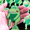 Green frog-shaped patches with a heart on a wooden surface.
