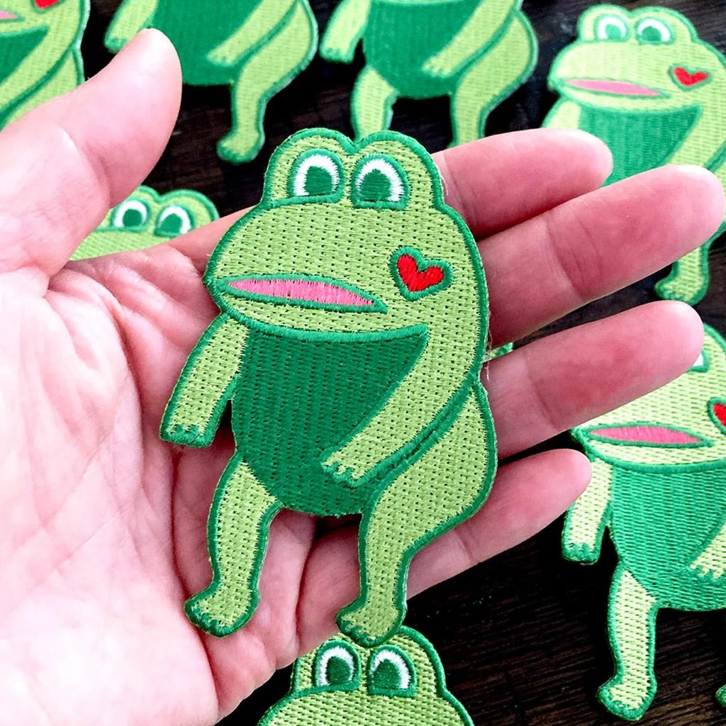 Green frog-shaped patches with a heart on a wooden surface.