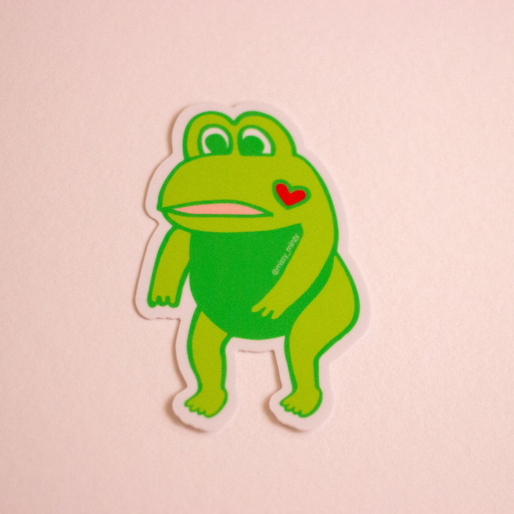 Green frog sticker with a red heart on a pink background