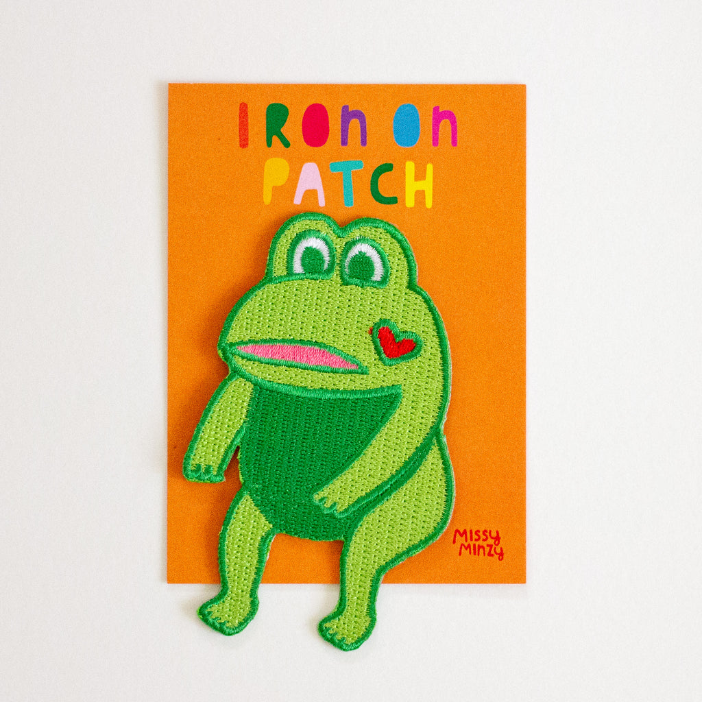 Green frog iron on patch with a heart on an orange card, brand 'Missy Minzy' visible.