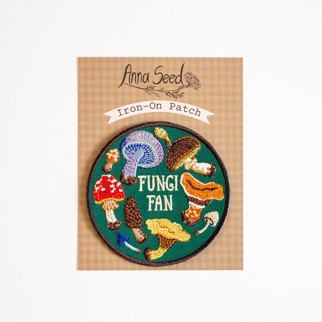 Iron-on patch with mushroom design and 'Fungi Fan' text on a cardboard backing, brand 'Anna Seed' visible.