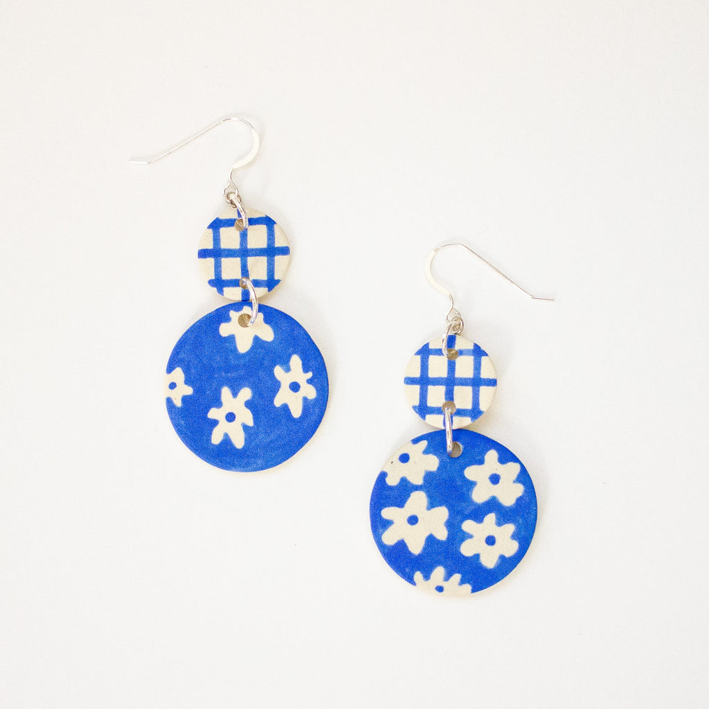 Blue earrings with white floral patterns on a white background