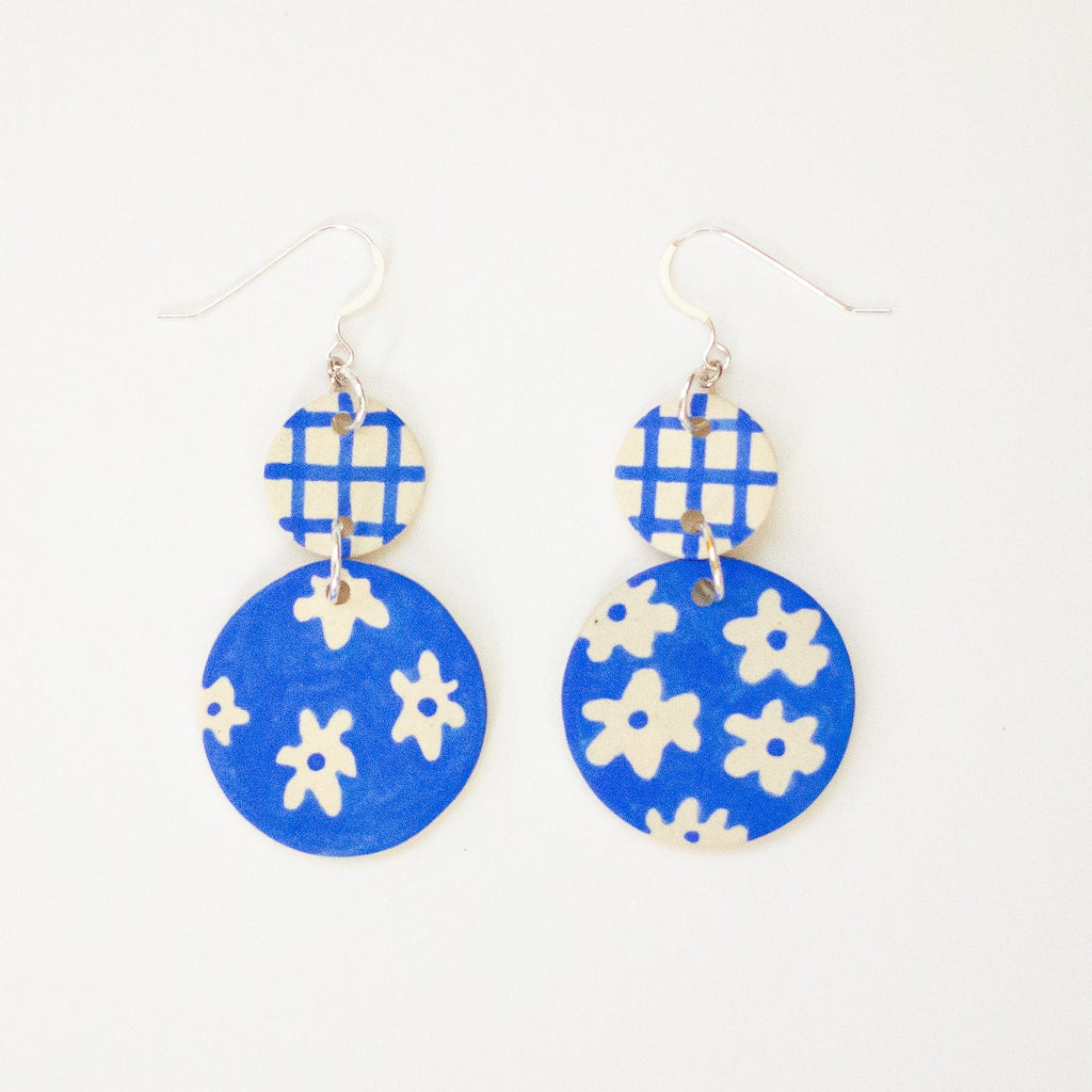 Blue earrings with white floral patterns on a white background
