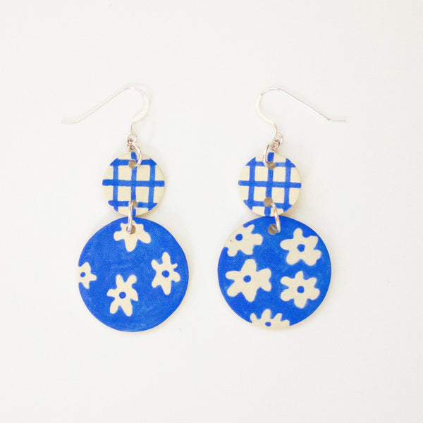 Blue earrings with white floral patterns on a white background