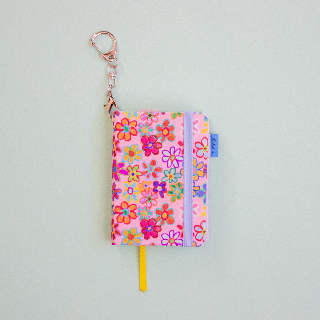 Floral-patterned keychain with a yellow ribbon bookmark on a light grey background