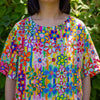 Person wearing a colorful floral linen top with a green leafy background