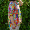 Person wearing a colorful floral linen top standing in front of green foliage