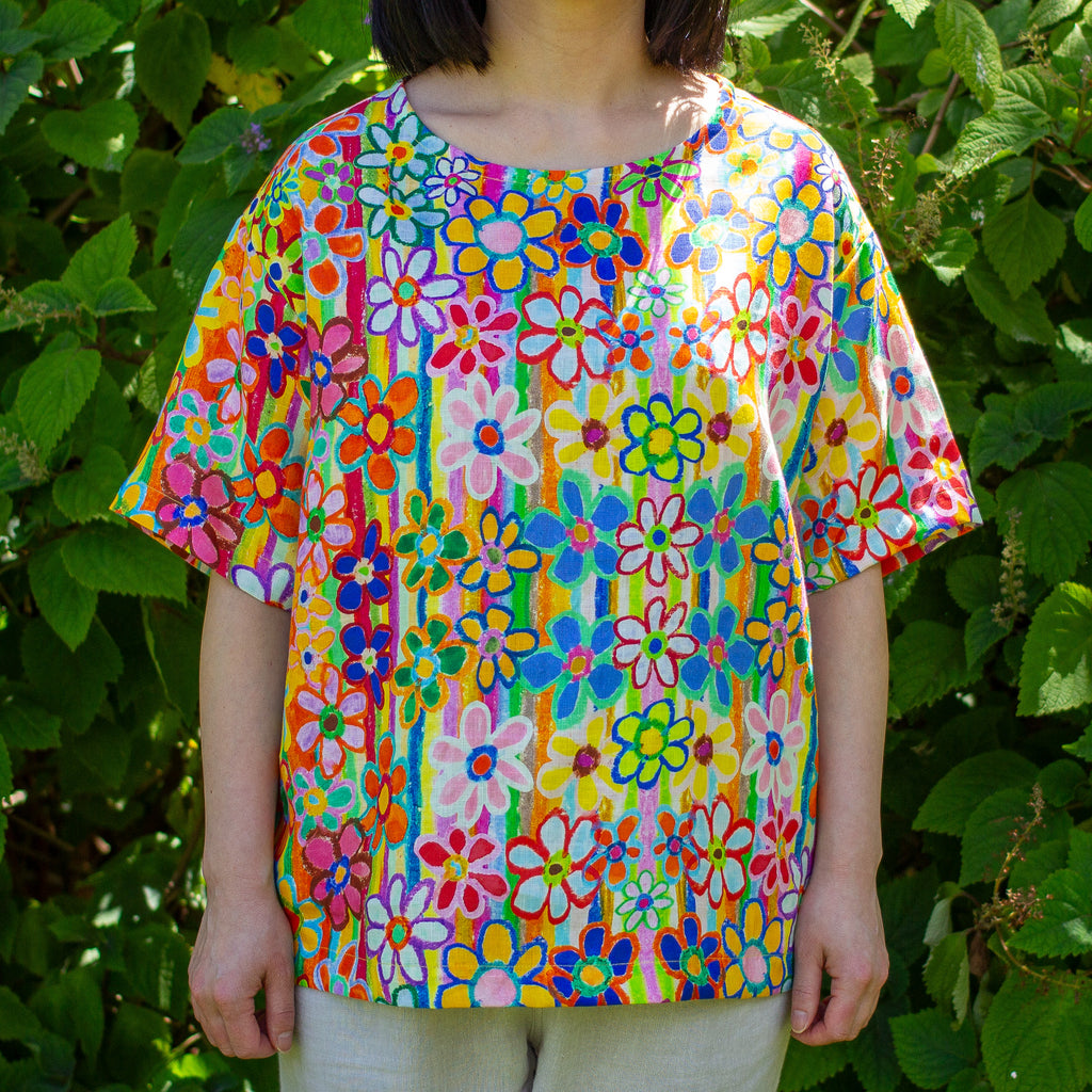 Child wearing a colorful floral linen shirt in front of green foliage
