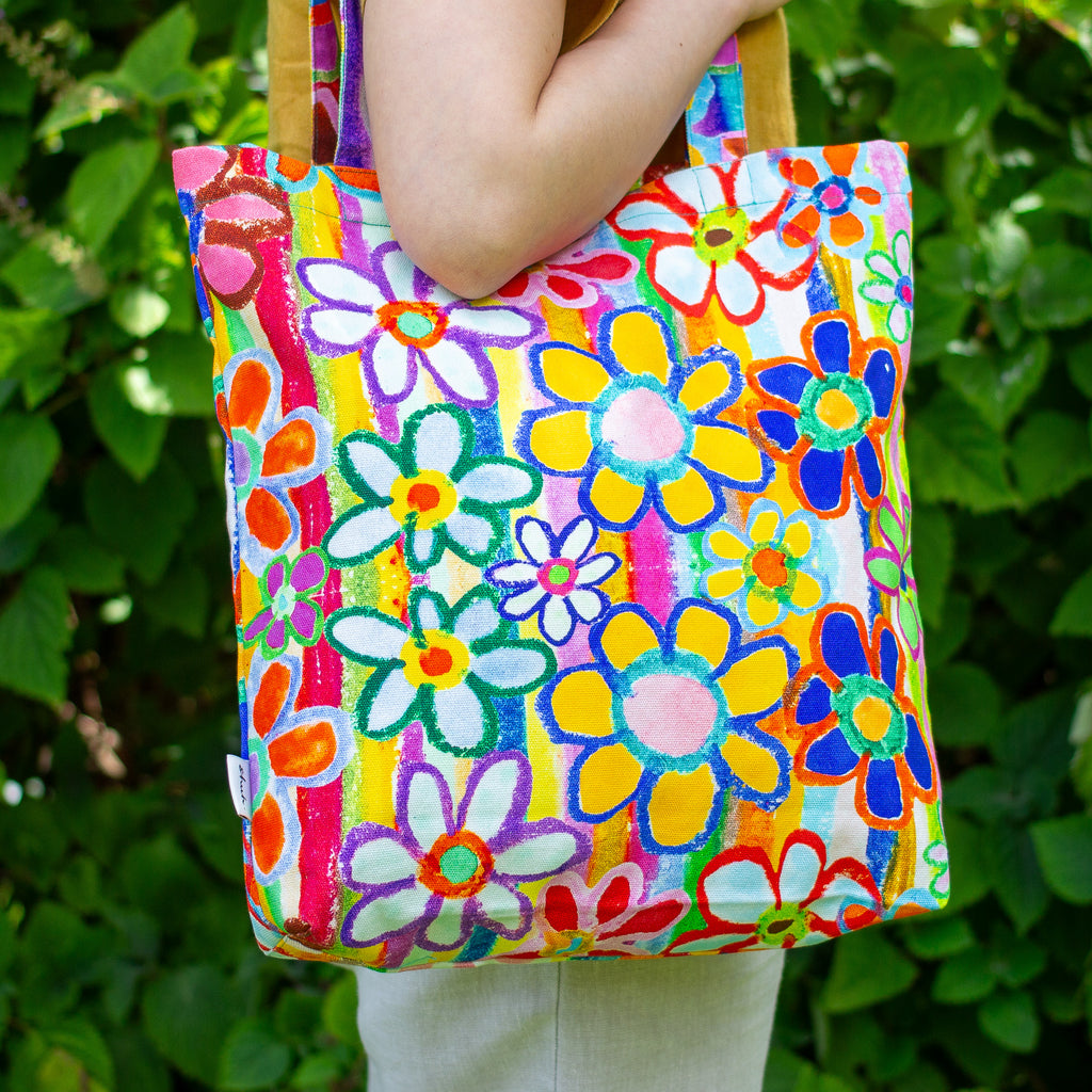 Colorful floral-patterned tote bag held by a person against a green leafy background