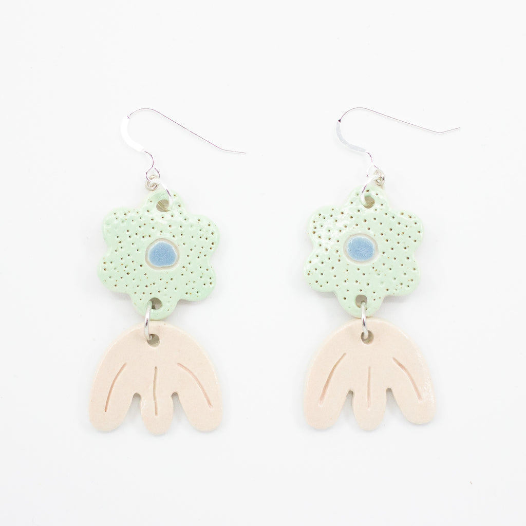 Picture features a closeup of two ceramic earrings with sterling silver hooks. Each earring has two ceramic beads, the first bead is light green coloured with polka dots and a blue highlight in the centre, in a daisy shape. The Second bead is tulip shaped in a pastel peach glaze. 