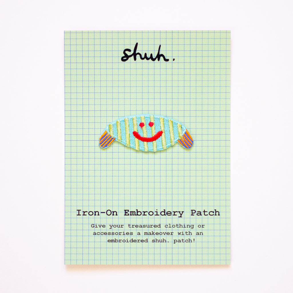 Iron-on embroidery patch with a smiley face design on a green checkered card.