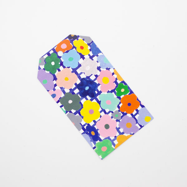 Closeup picture of the flower gift tag. Print has hand drawn daisies, over a blue and white chequered background. Flowers are multicoloured. 