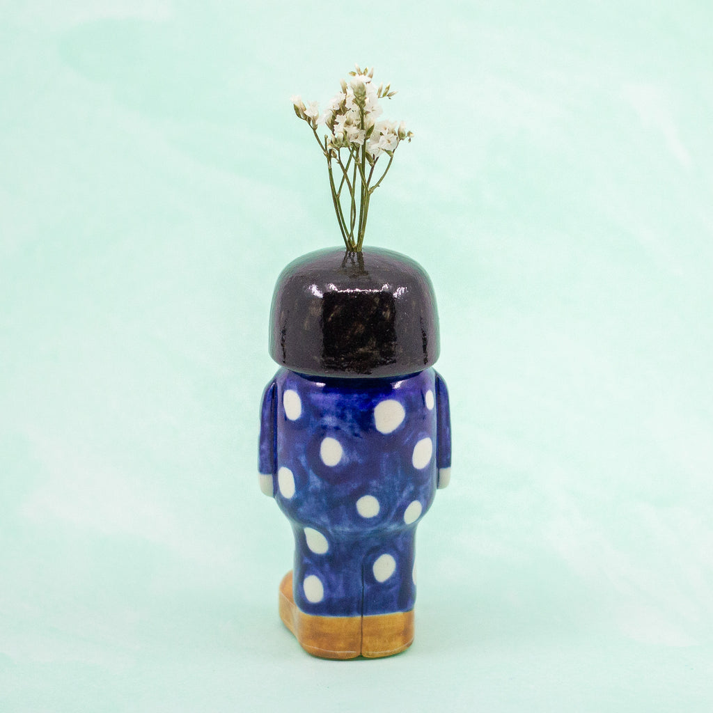 Decorative ceramic figurine shaped like a person with polka dot pattern outfit on a light green background