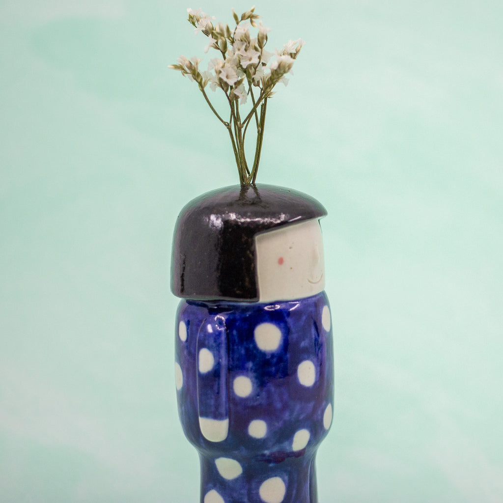 Ceramic figurine with polka dot design outfit and black hair on a light green background