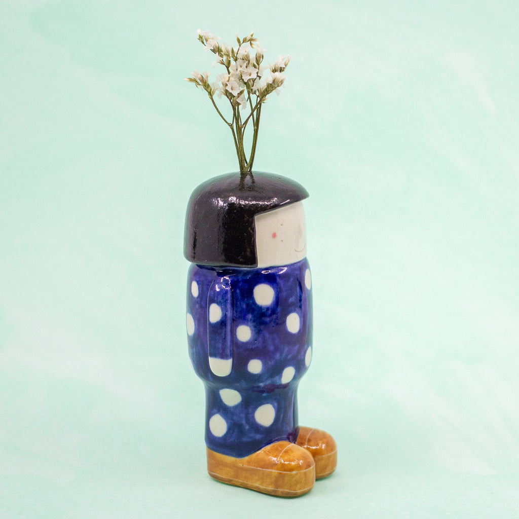 Ceramic figurine shaped like a person with polka dot pattern outfit and flowers on a light green background