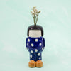 Ceramic vase shaped like a person with polka dot outfit and bob hair on light blue background