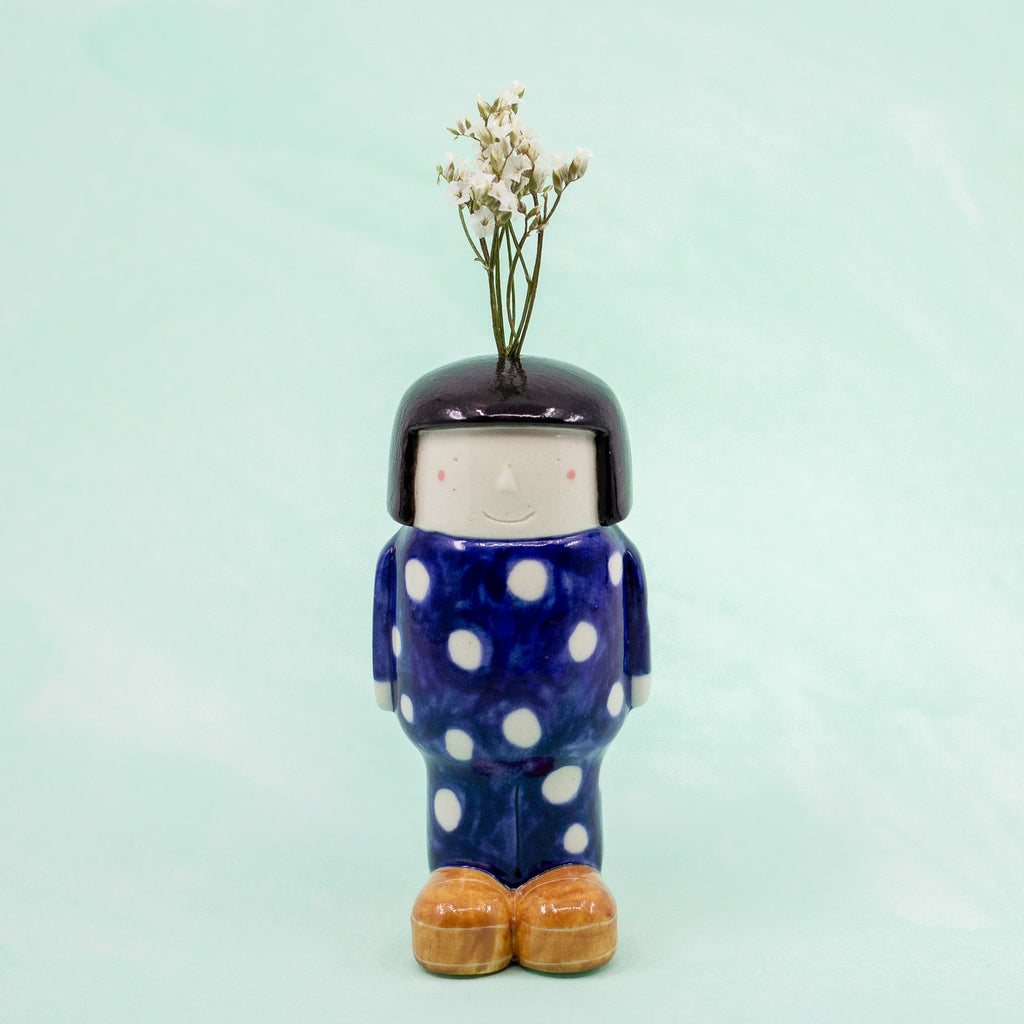 Ceramic vase shaped like a person with polka dot outfit and bob hair on light blue background
