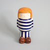 Ceramic figurine of a person with striped shirt and orange hair on a gray background
