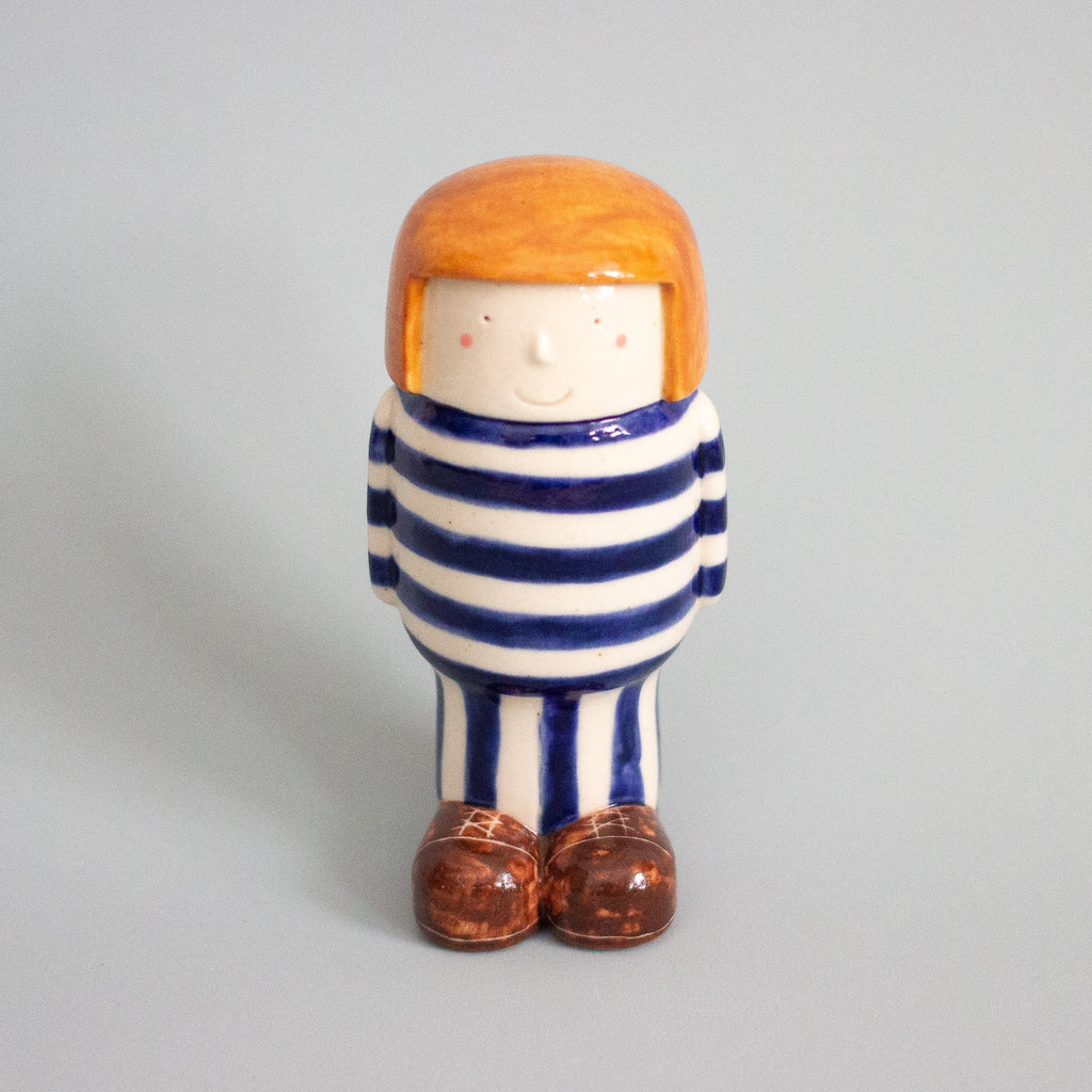 Ceramic figurine of a person with striped shirt and orange hair on a gray background