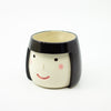 Ceramic mug shaped like a face with black hair on a white background