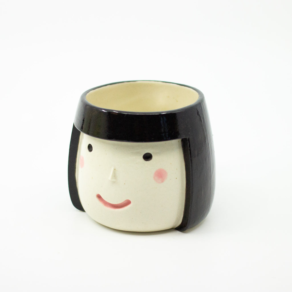 Ceramic mug shaped like a face with black hair on a white background