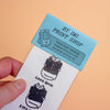 A hand holds a printed card against a peach background. The top portion is light blue with the text 'BY IMI PRINT SHOP' and a small illustration of a flip phone.