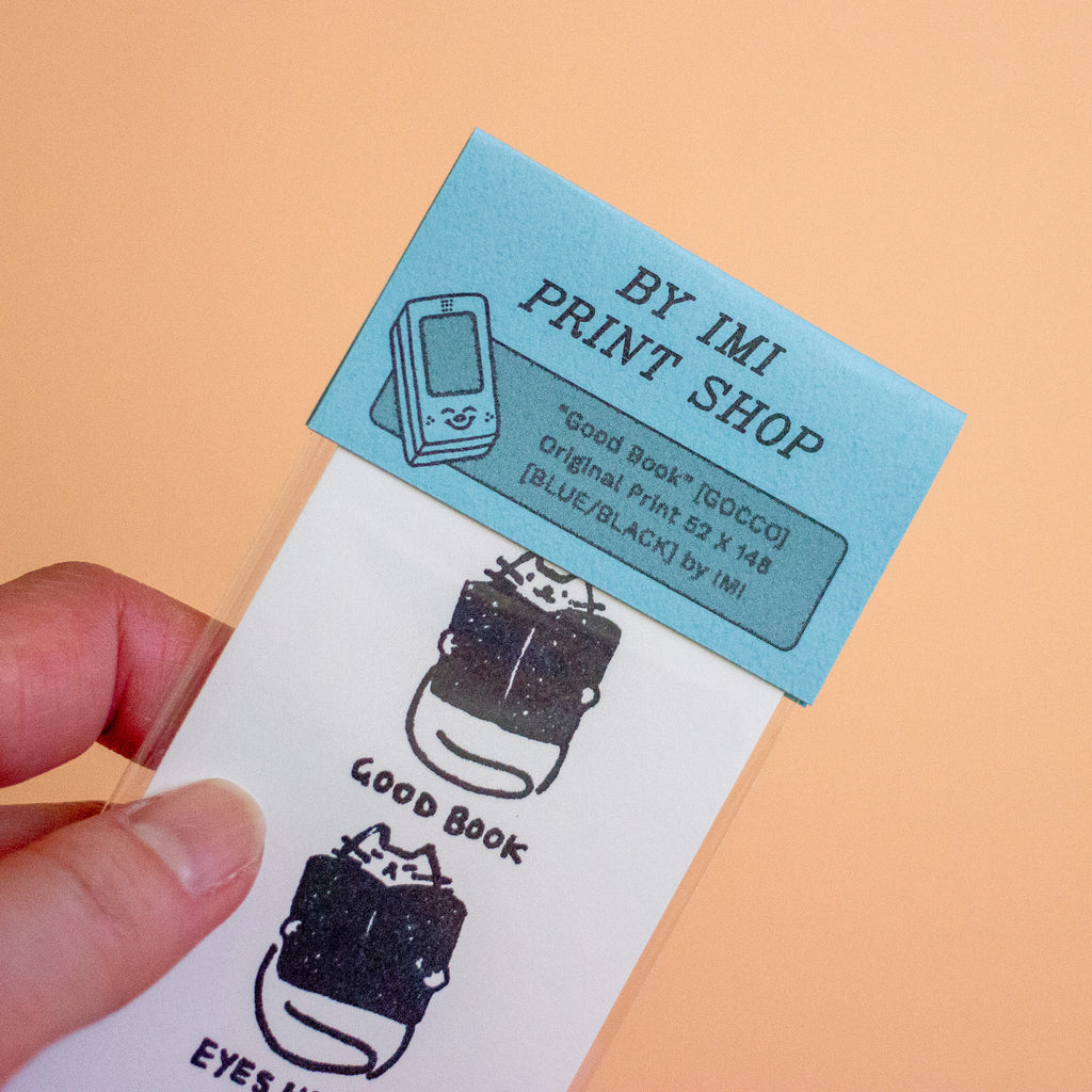 A hand holds a printed card against a peach background. The top portion is light blue with the text 'BY IMI PRINT SHOP' and a small illustration of a flip phone.