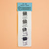 A vertical white paper bookmark or card with a light blue header reading 'BY IMI PRINT SHOP,' featuring four small black-and-white illustrations of a book with humorous captions: 'GOOD BOOK,' 'EYES HEAVY,' 'FEELS NICE,' and 'SLAP!,' shown on a peach background.