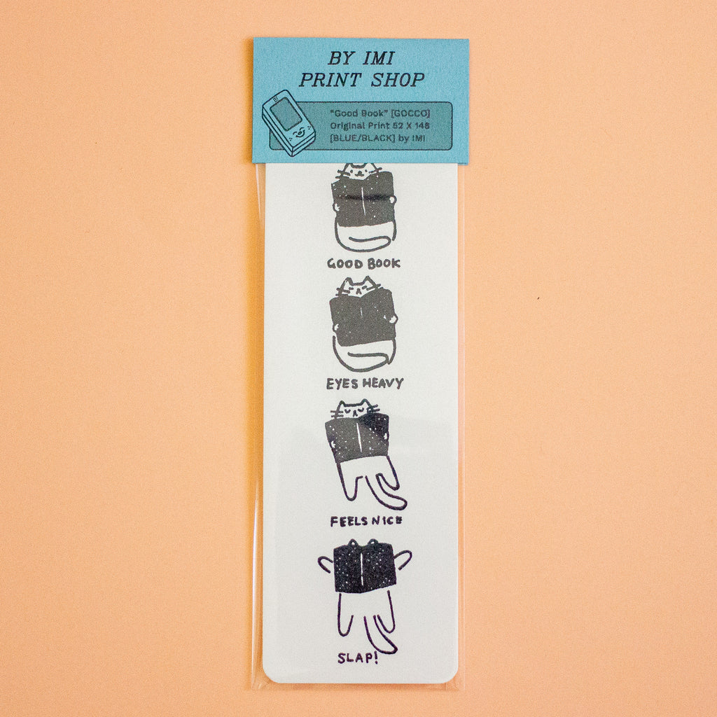 A vertical white paper bookmark or card with a light blue header reading 'BY IMI PRINT SHOP,' featuring four small black-and-white illustrations of a book with humorous captions: 'GOOD BOOK,' 'EYES HEAVY,' 'FEELS NICE,' and 'SLAP!,' shown on a peach background.