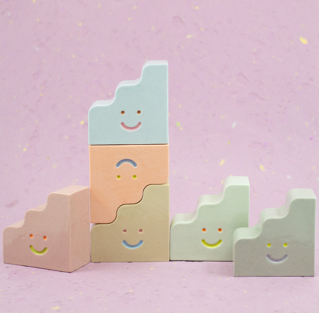 Set of pastel-colored ceramic figures with smiley faces on a pink background